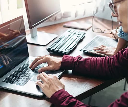 A professional typing at a laptop beside a second monitor