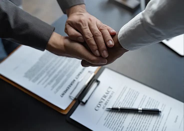 Hands joined over a signed contract agreement